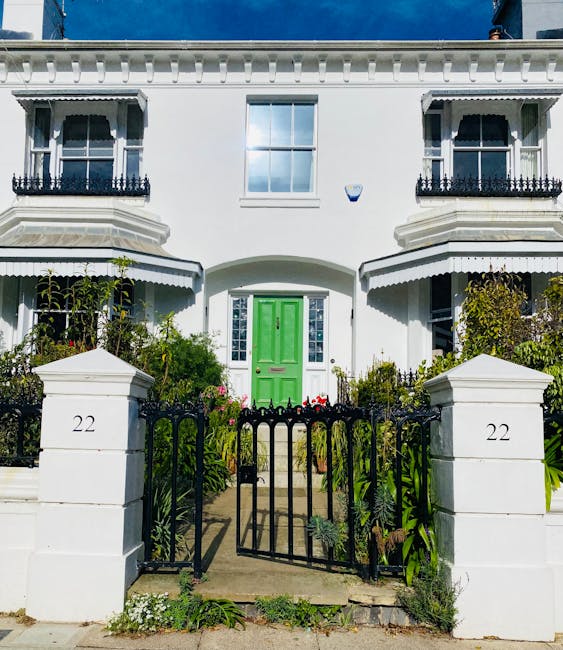 The image depicts a charming Victorian terrace house with a white façade, featuring decorative mouldings and black wrought-iron balcony railings on the upper floor windows. The house has a bright gre
