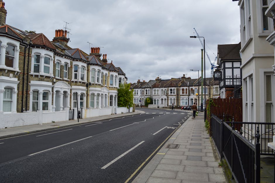 The image depicts a charming Victorian terrace house with a white façade, featuring decorative mouldings and black wrought-iron balcony railings on the upper floor windows. The house has a bright gre